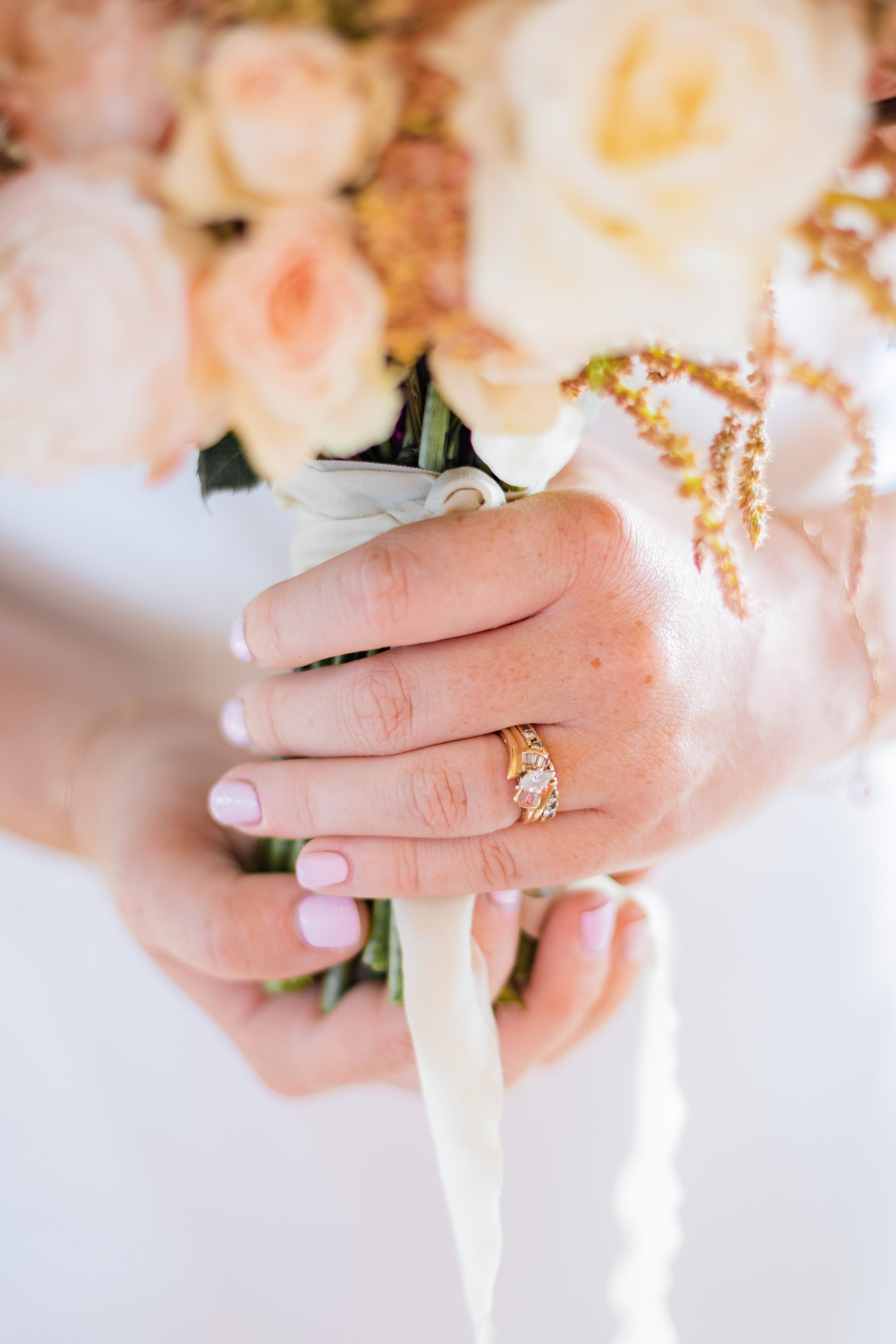 Wedding hand with engagement ring holding soft pastel rose bouquet