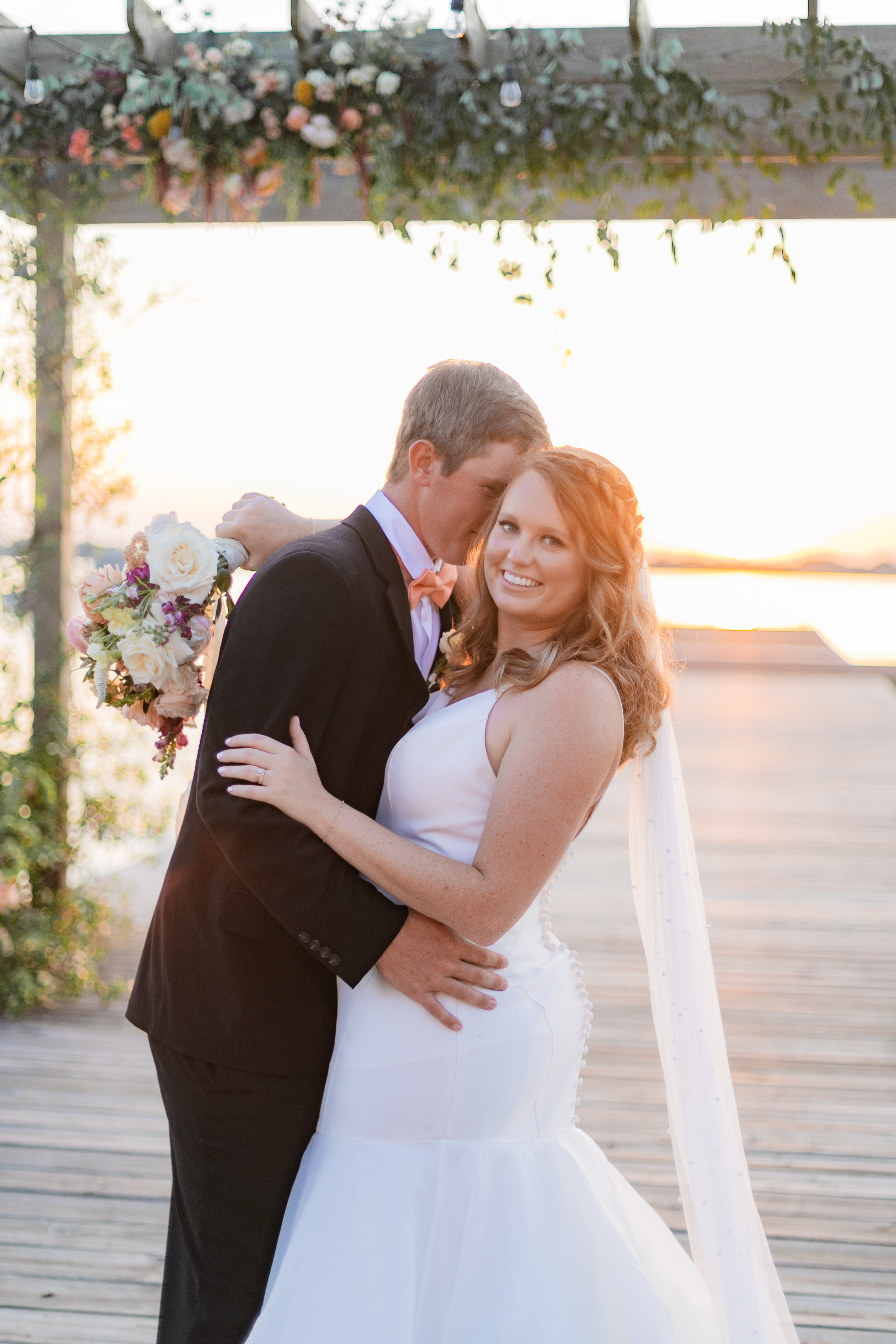Newlyweds embrace at sunset under floral-decorated wedding arch