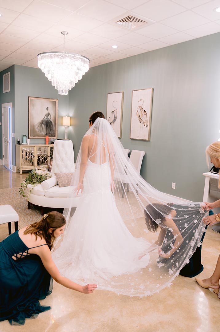 Bride in white dress getting ready, with long lace veil and bridesmaids