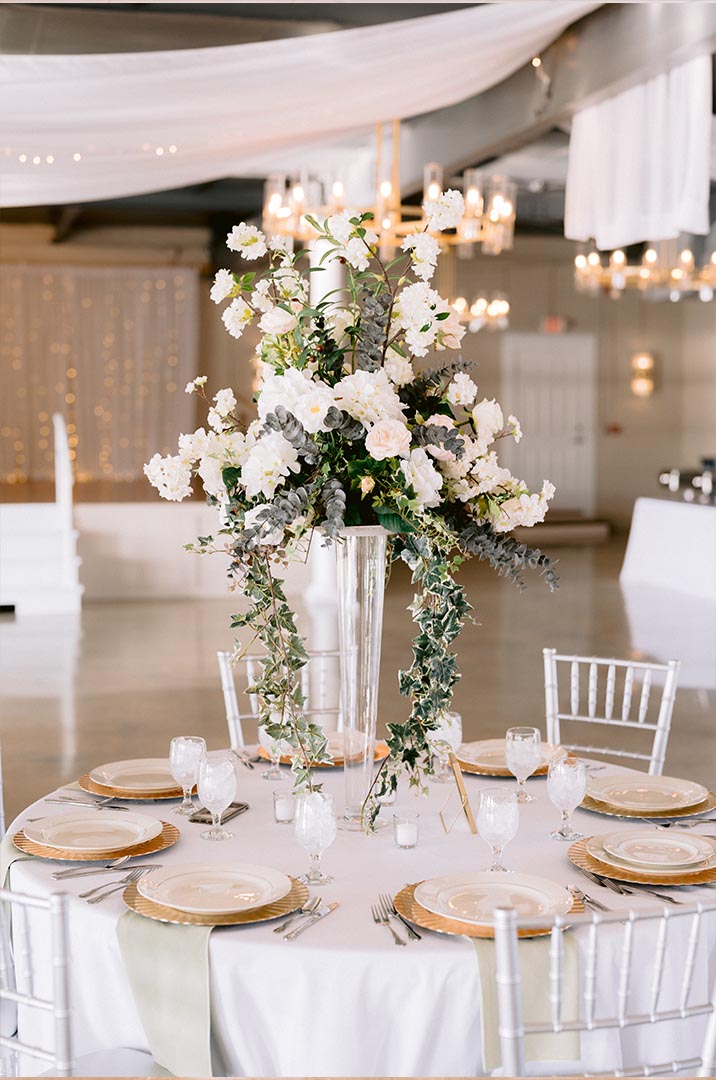 Elegant white wedding table setting with tall floral centerpiece and chandeliers