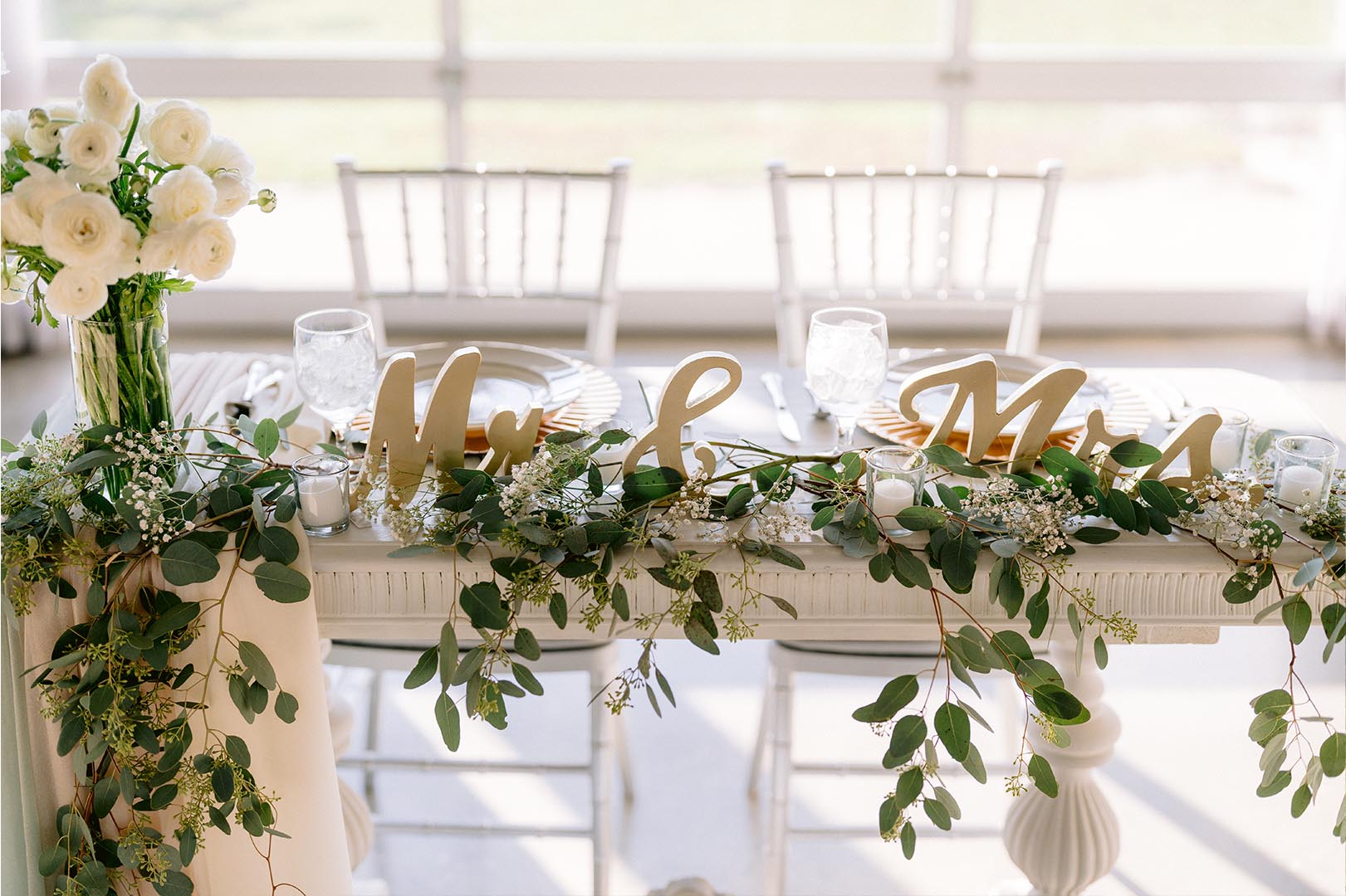 Wedding table decorated with white flowers, greenery, and Mr and Mrs signs