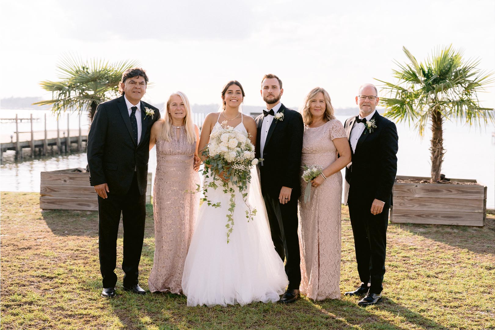 Wedding party posing together by pier with palm trees and waterfront