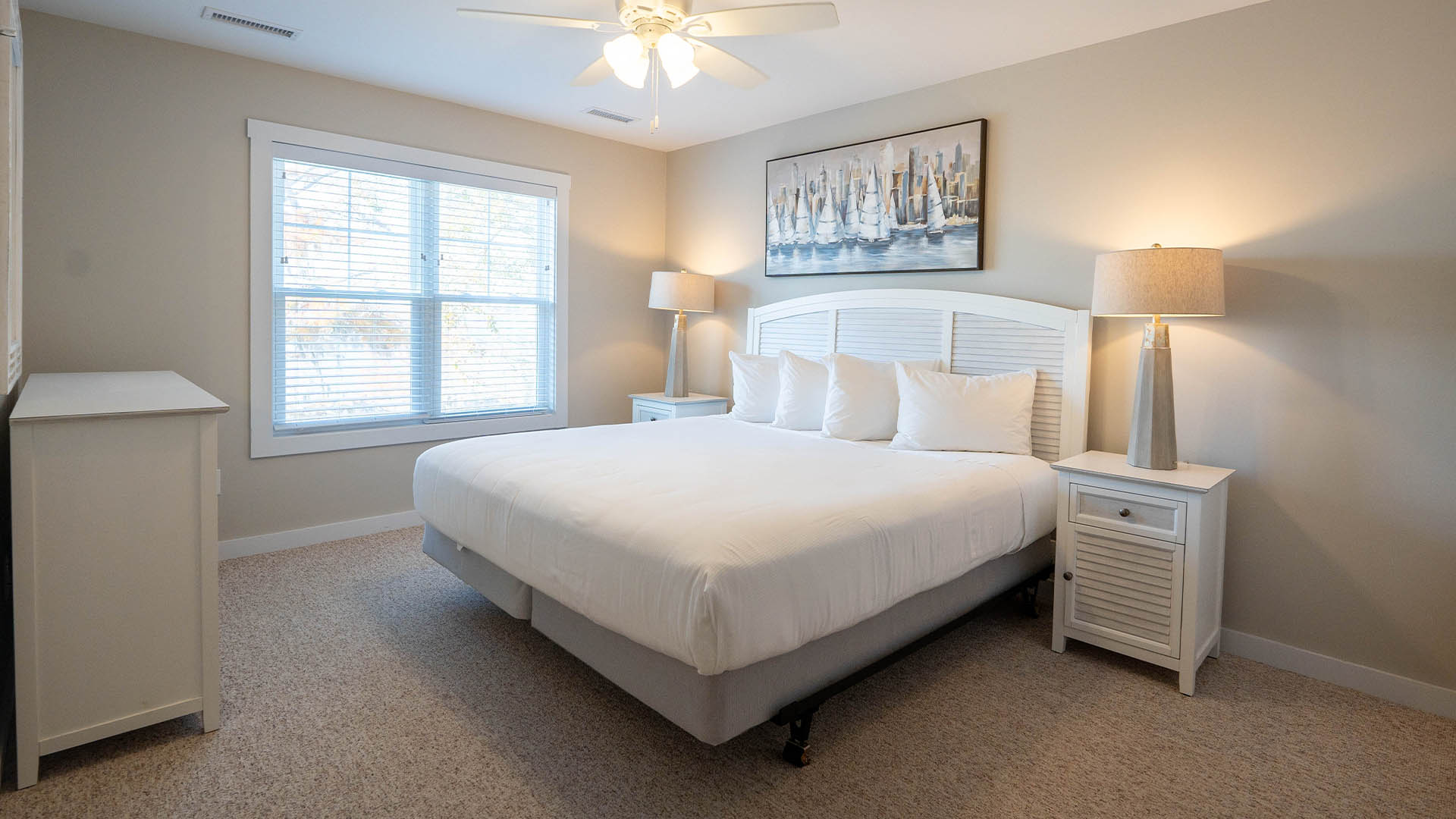 Bright, clean bedroom with white bed, nautical art, and soft lighting