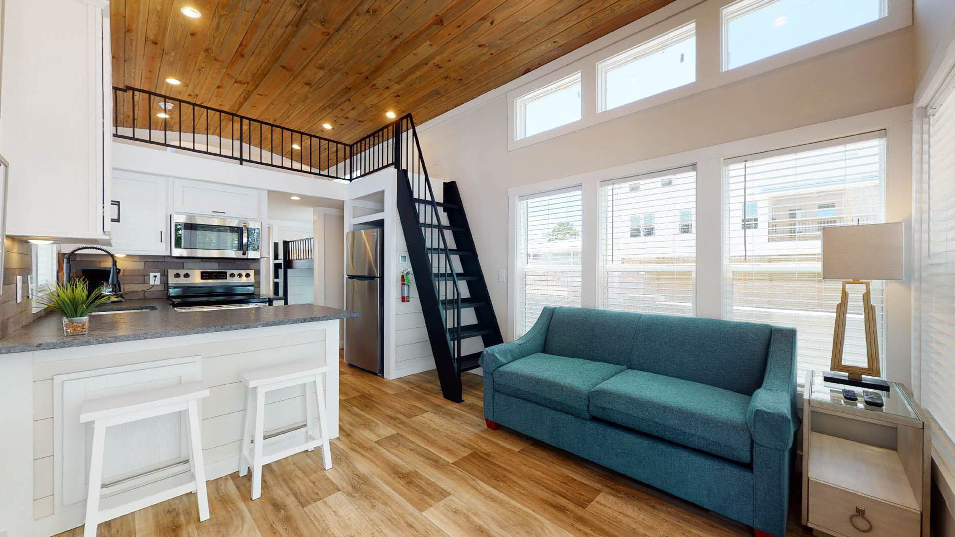 Modern tiny house interior with loft, kitchen, and teal sofa