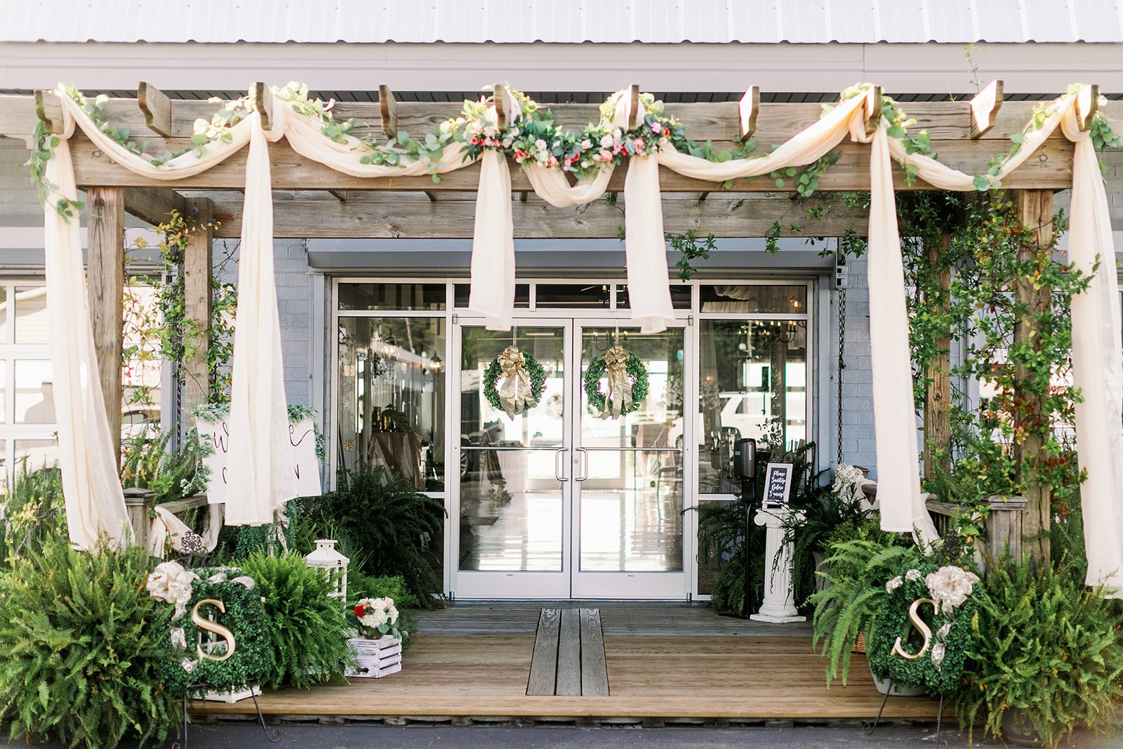 Elegant wedding venue entrance with draped fabric, greenery, and floral wreaths