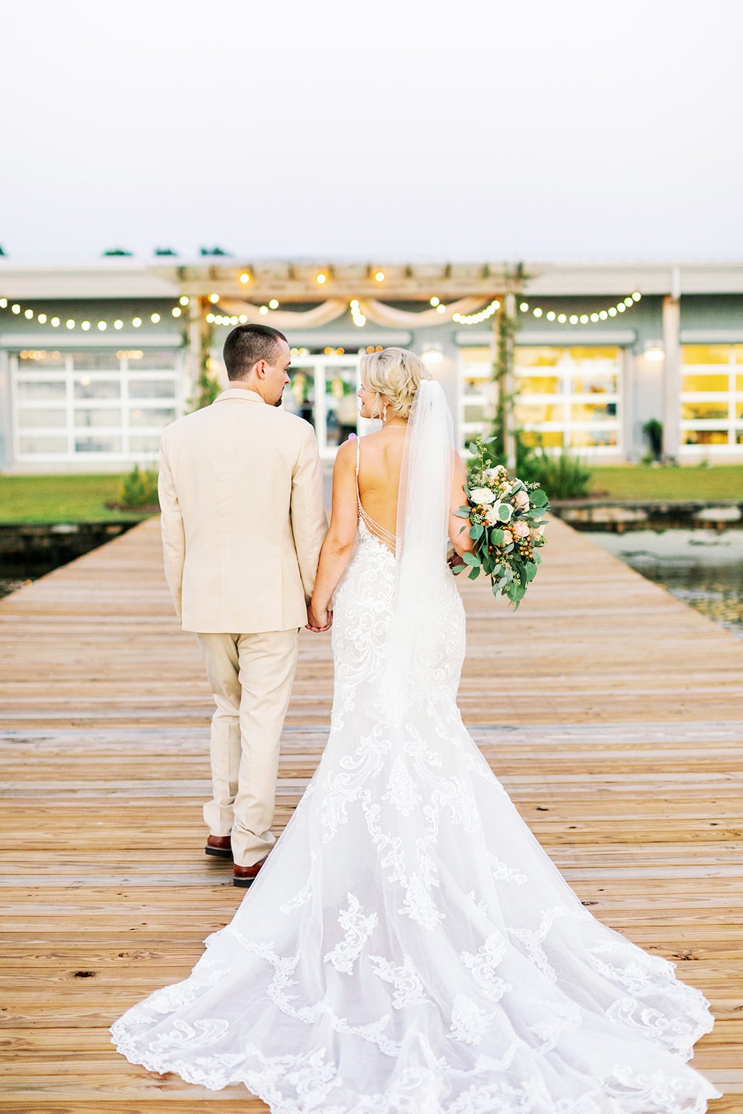 Wedding couple holding hands on wooden pier with string lights