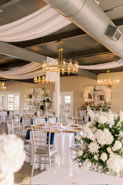 Elegant wedding reception with white flowers, chandeliers, and draped ceiling