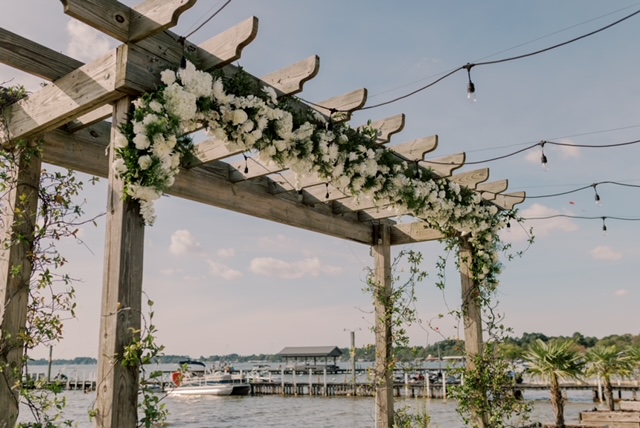 Wooden pergola decorated with white flowers overlooking waterfront marina