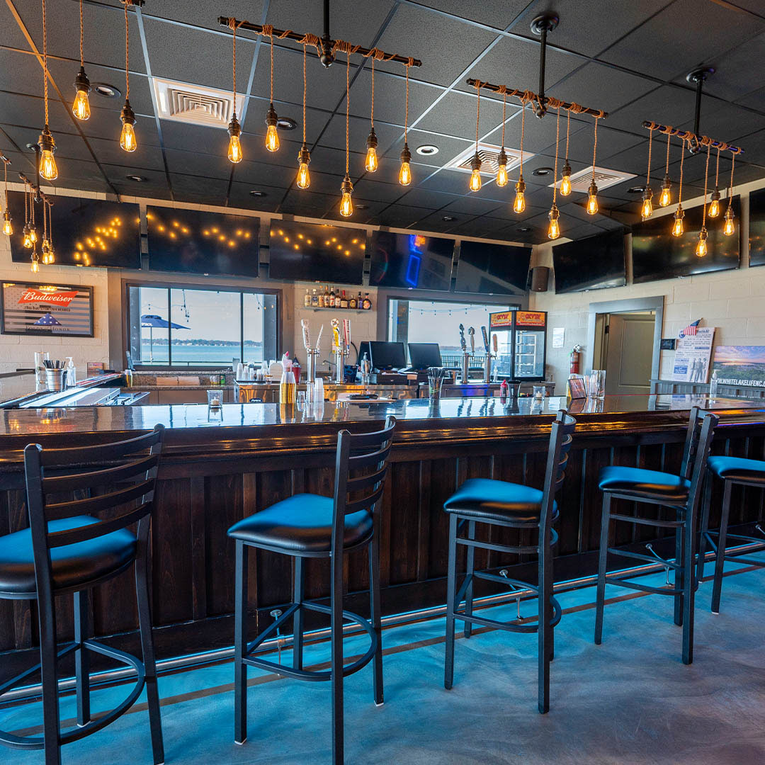 Bar interior with vintage Edison bulbs, blue barstools, and waterfront view