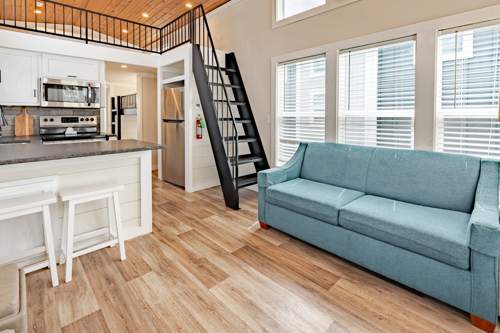 Modern tiny house interior with loft, blue sofa, and wood flooring