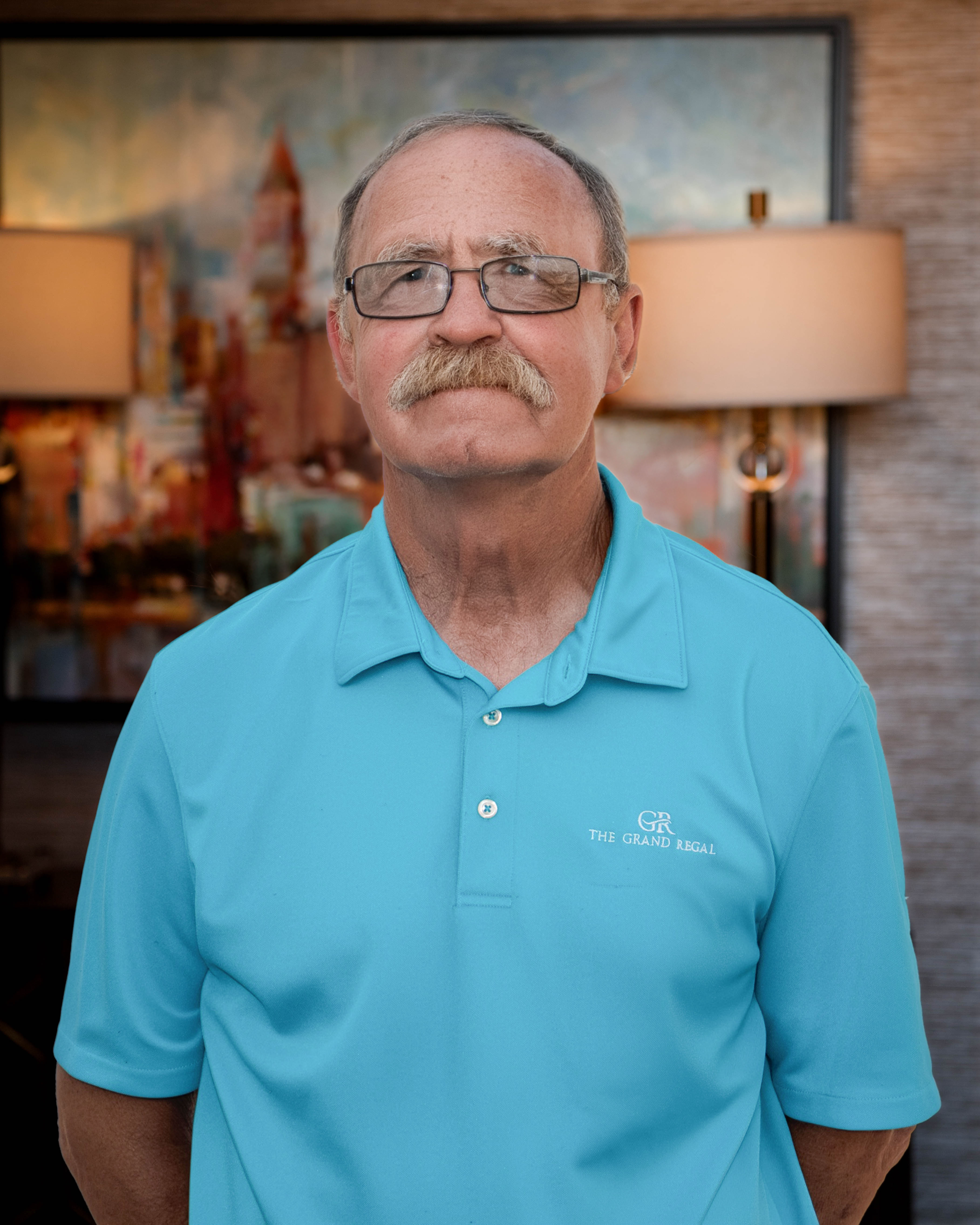 Older gentleman in blue polo shirt with glasses and mustache
