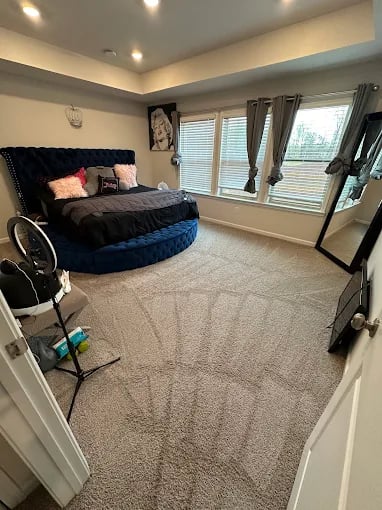 Spacious bedroom with round blue bed, large mirror, and window blinds