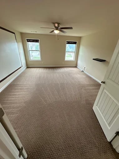Empty room with beige carpet, two windows, and ceiling fan