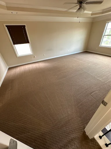 Empty room with brown carpet, windows, and ceiling fan