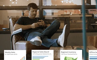 A man sitting in a chair, using a laptop on his lap and holding a phone in his hand.