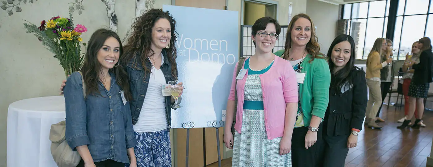 Five women taking a photo in front of a panel.