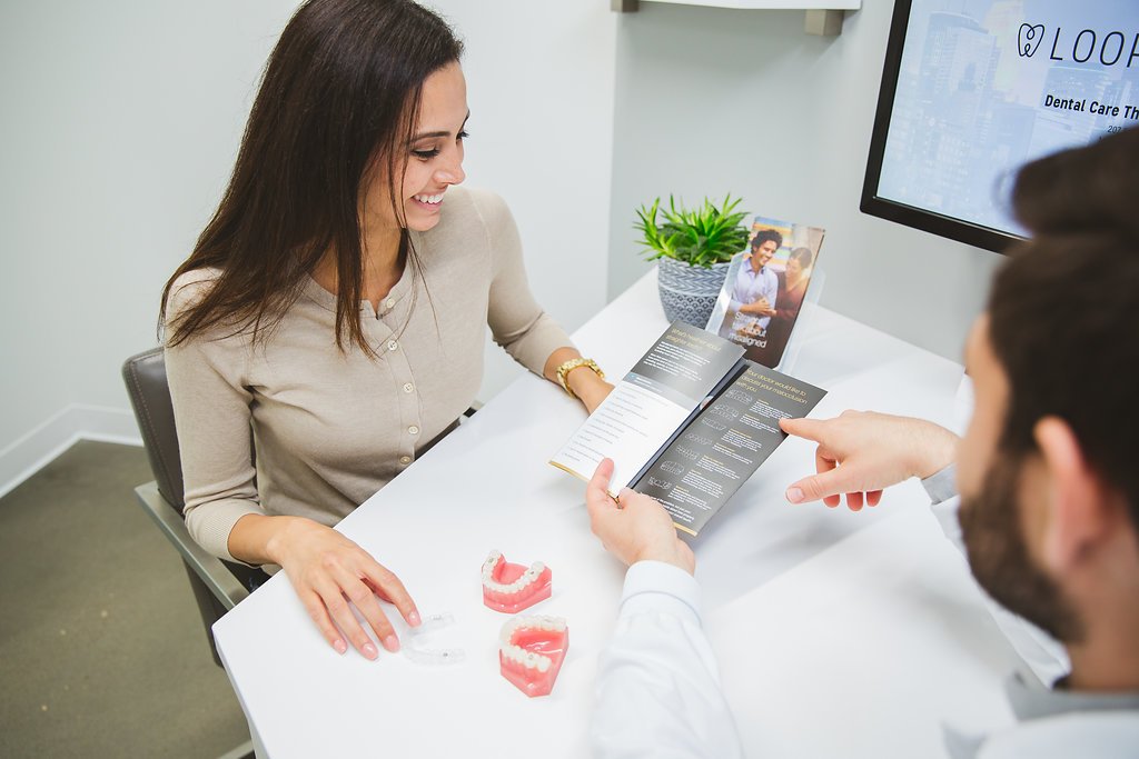 Dentist and female patient seated across a consultation table at Loop Dental, reviewing dental models and brochures while discussing a treatment plan