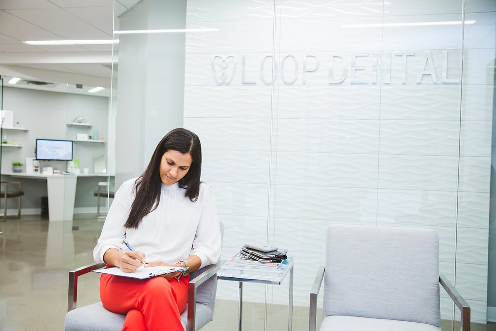 A patient at Loop Dental filling out intake forms while seated in the waiting area, surrounded by modern white furniture and natural lighting