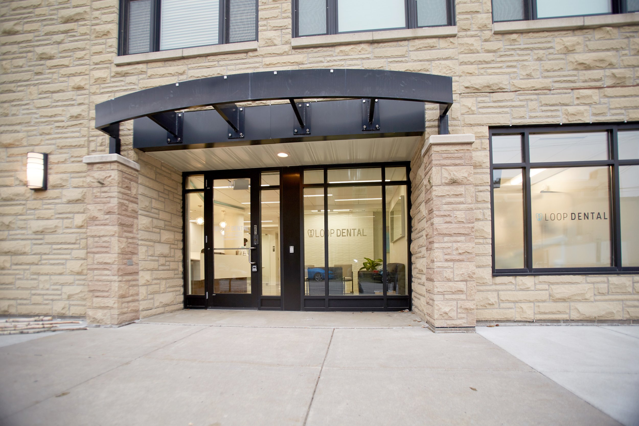Front entrance of Loop Dental with a curved glass awning, sliding glass doors, and clear signage welcoming patients into the clinic