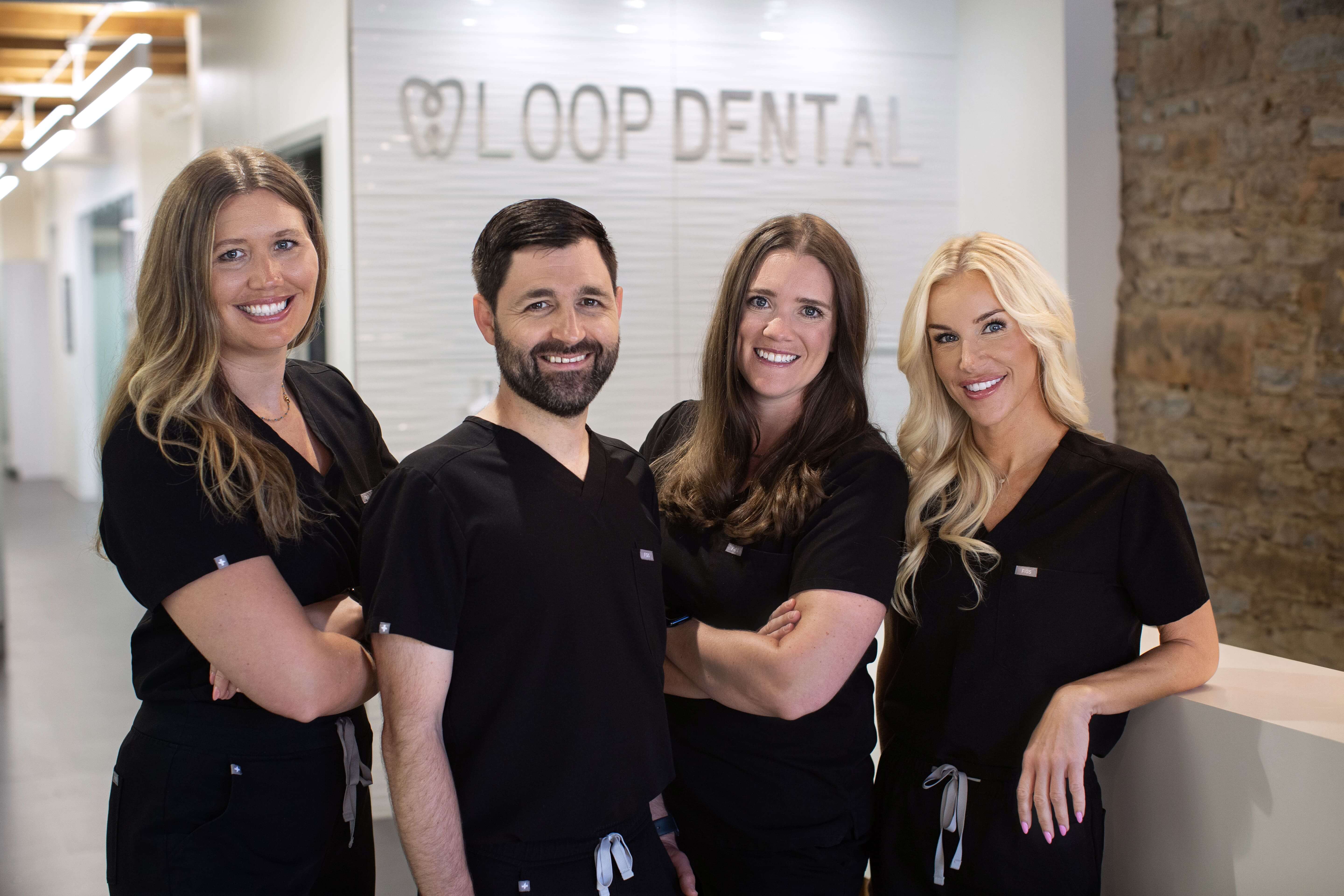 Dr. David Bates, owner of Loop Dental, and Dr. Katie Hannon standing together in front of a wood backdrop, both smiling and wearing professional attire