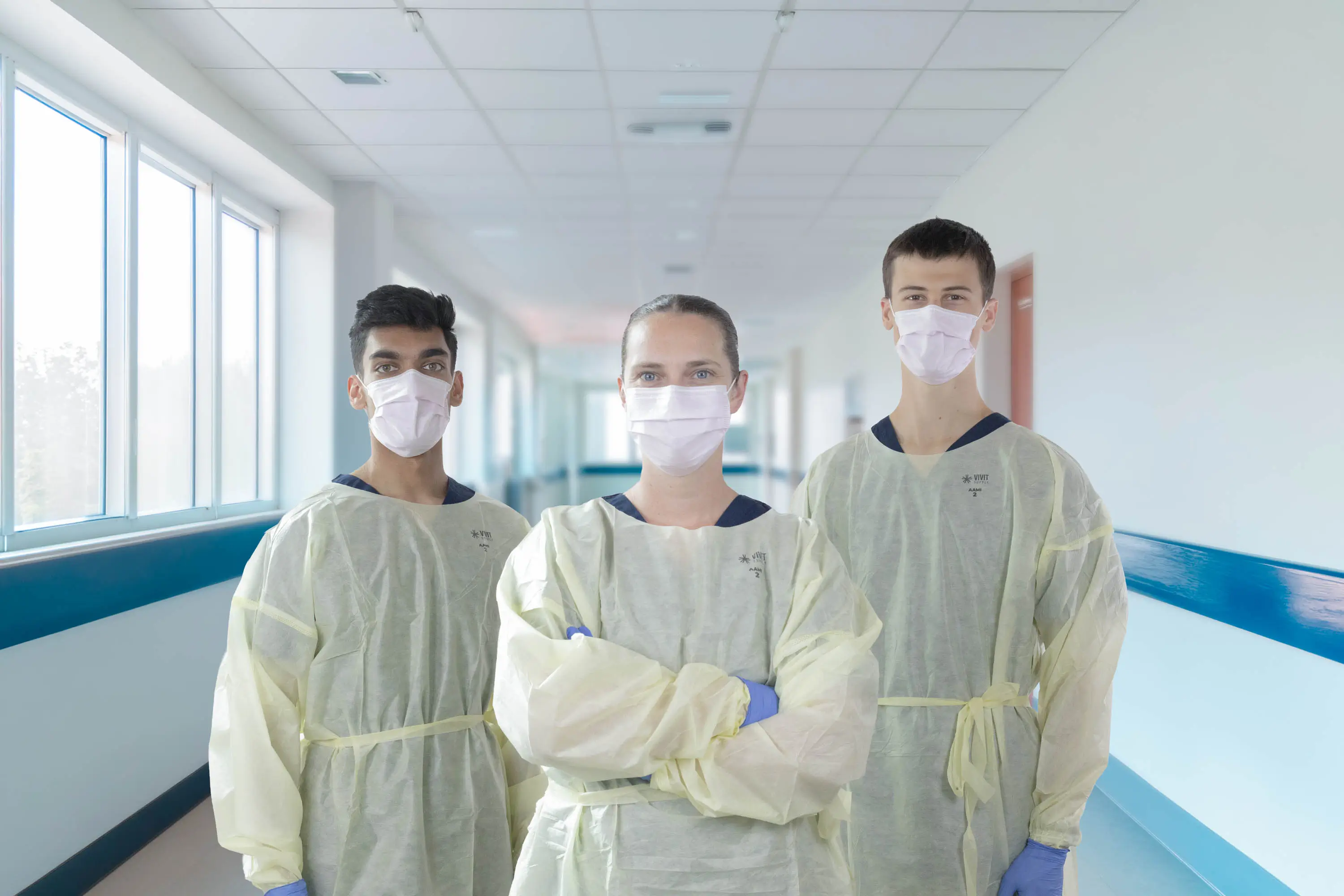 Three healthcare workers in isolation gowns wearing pink medical face masks