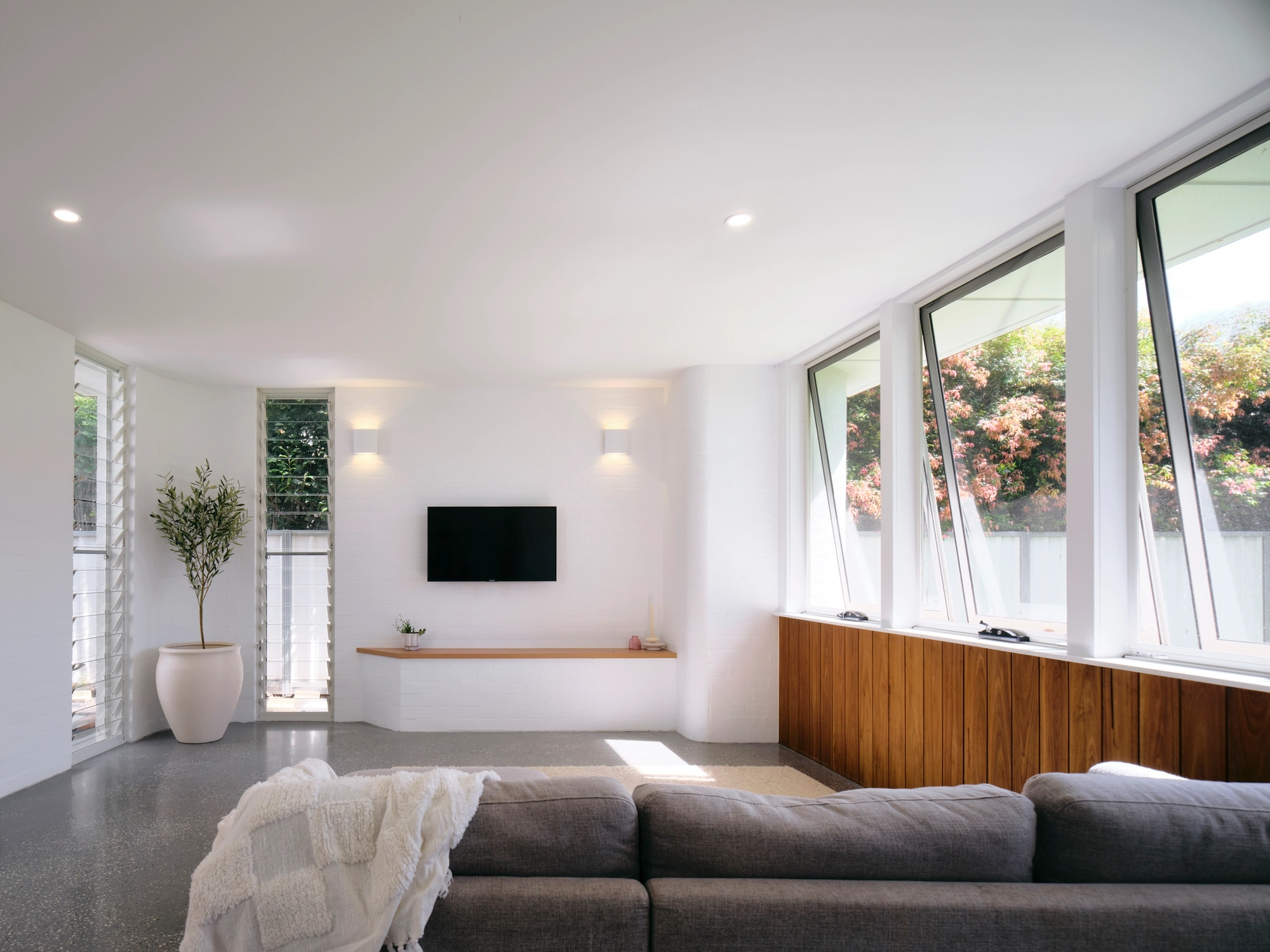 Image of a loungeroom with white walls, a great lounge facing a tv and three large windows on the right hand side