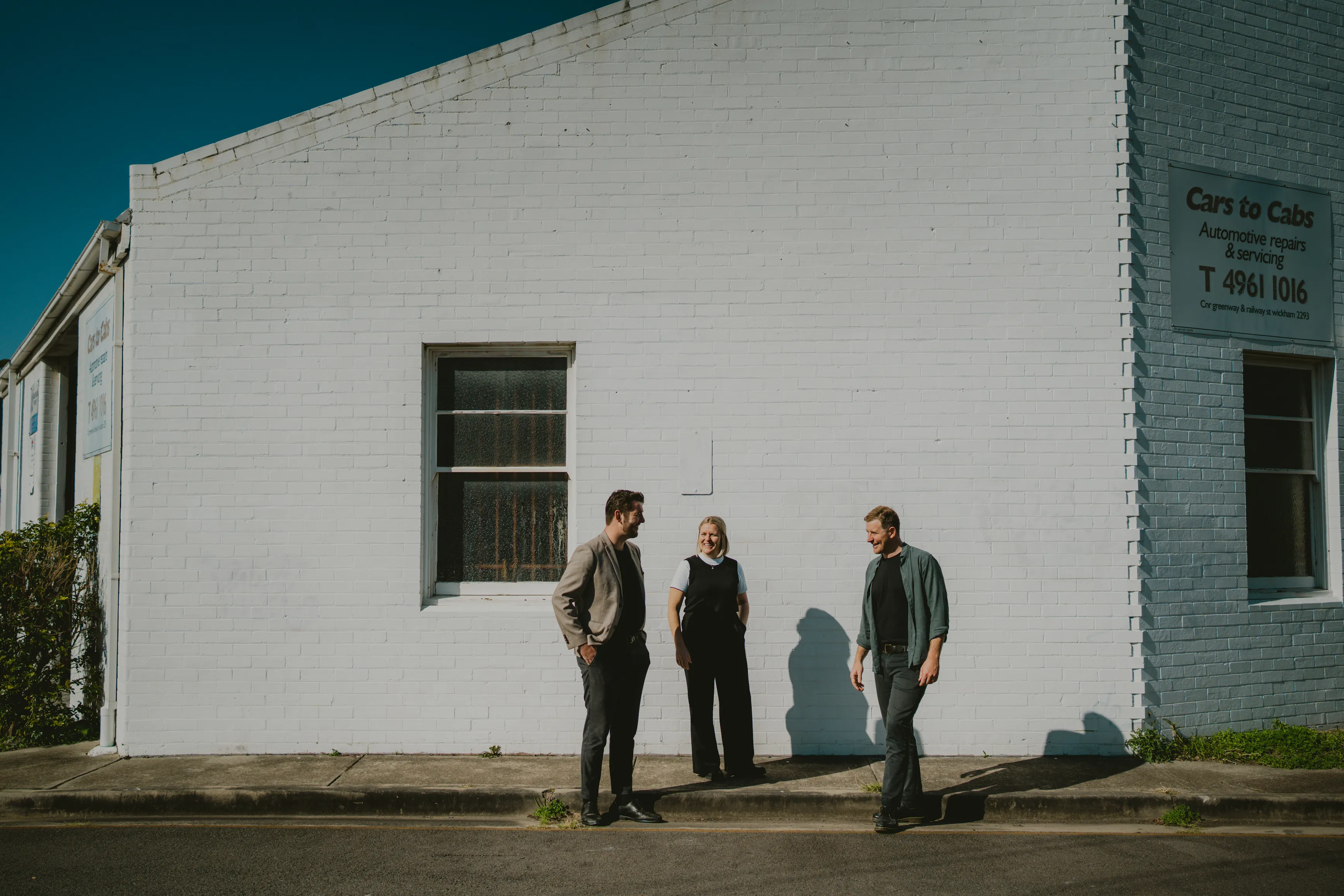 Three people standing in front of white brick building