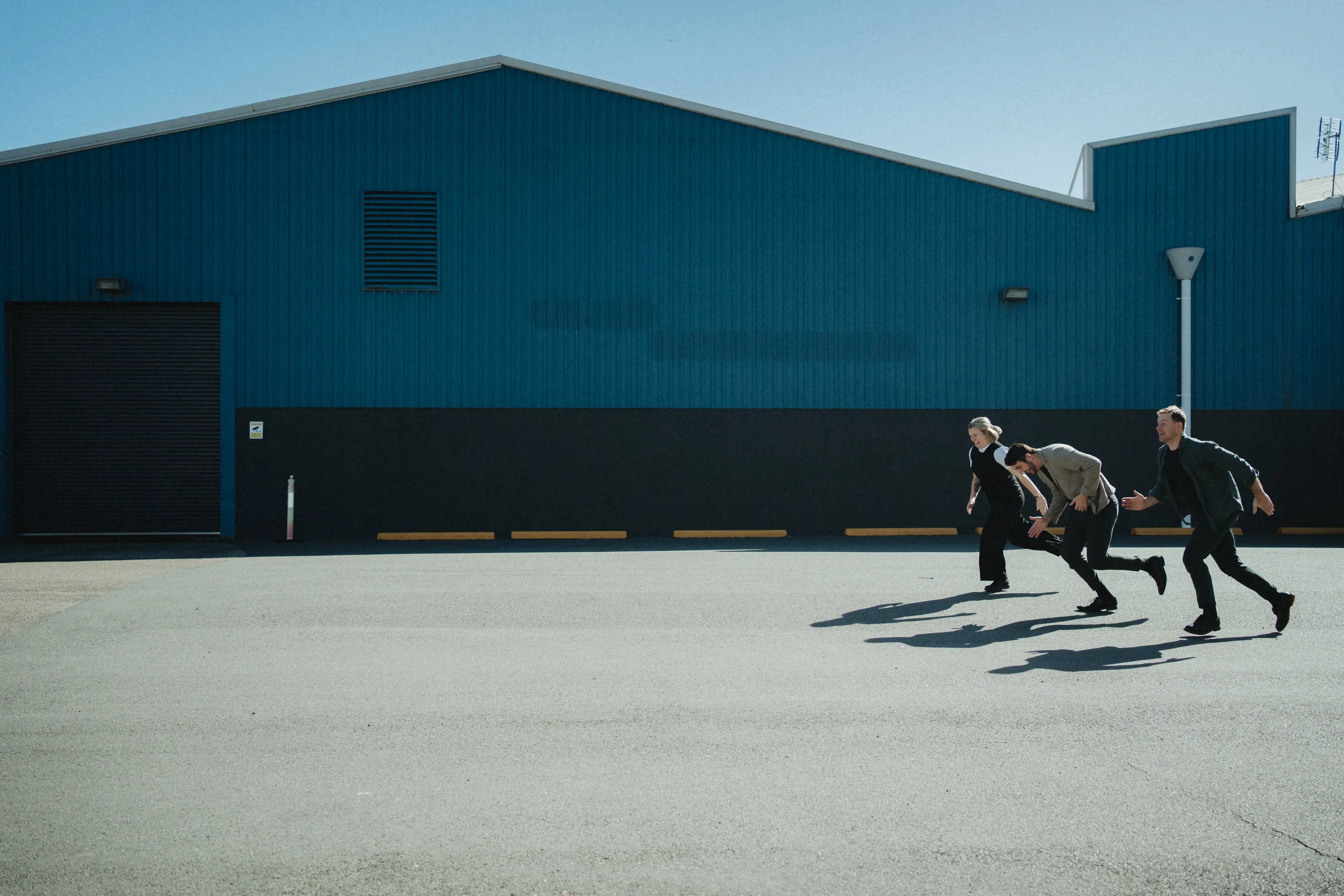 Three people running in front of industrial shed