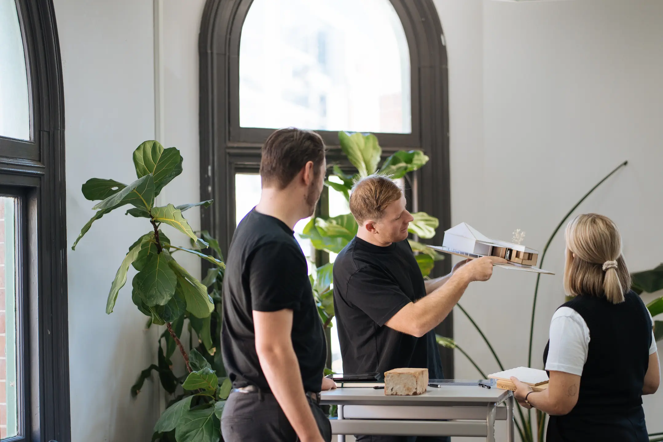Architect showing model of house to two clients with green plants in background