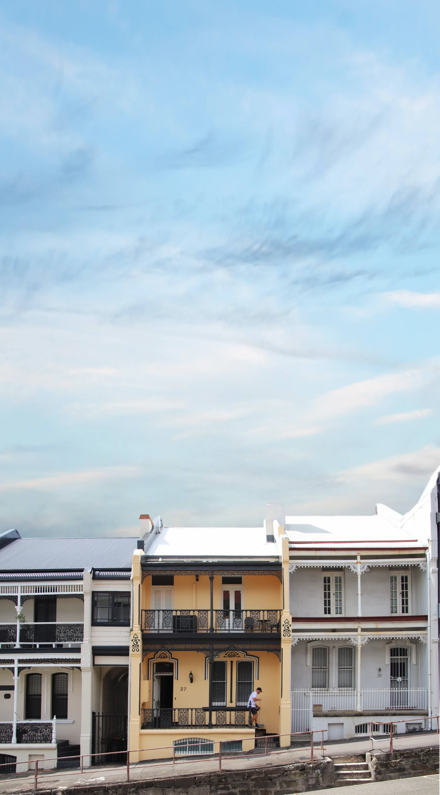 Yellow terrace house with man sweeping balcony with lots of blue sky above