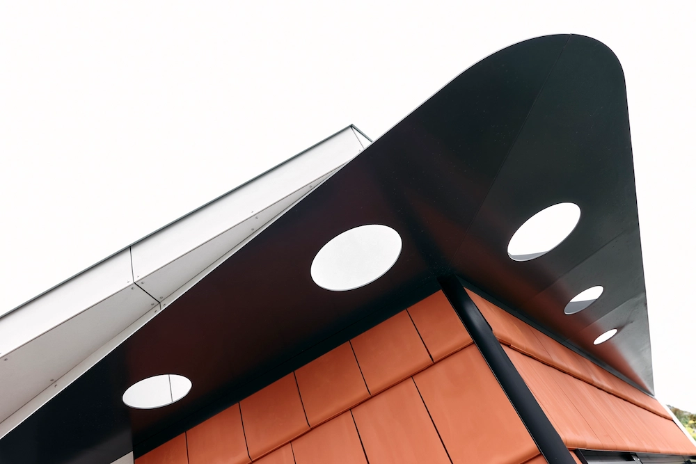 Modern building corner with a black overhang featuring circular cutouts above orange paneling.
