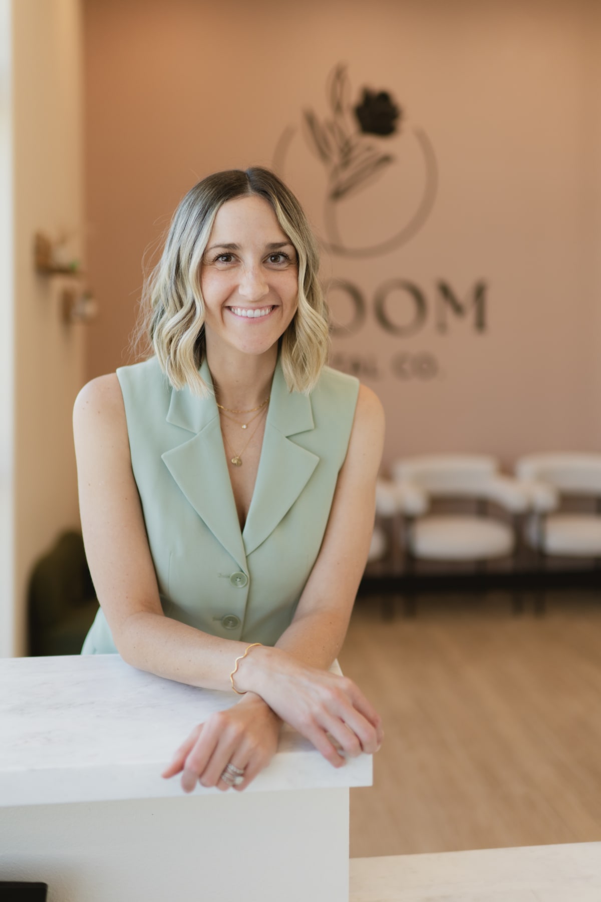 Woman in light green top leaning against white counter in modern dental office.