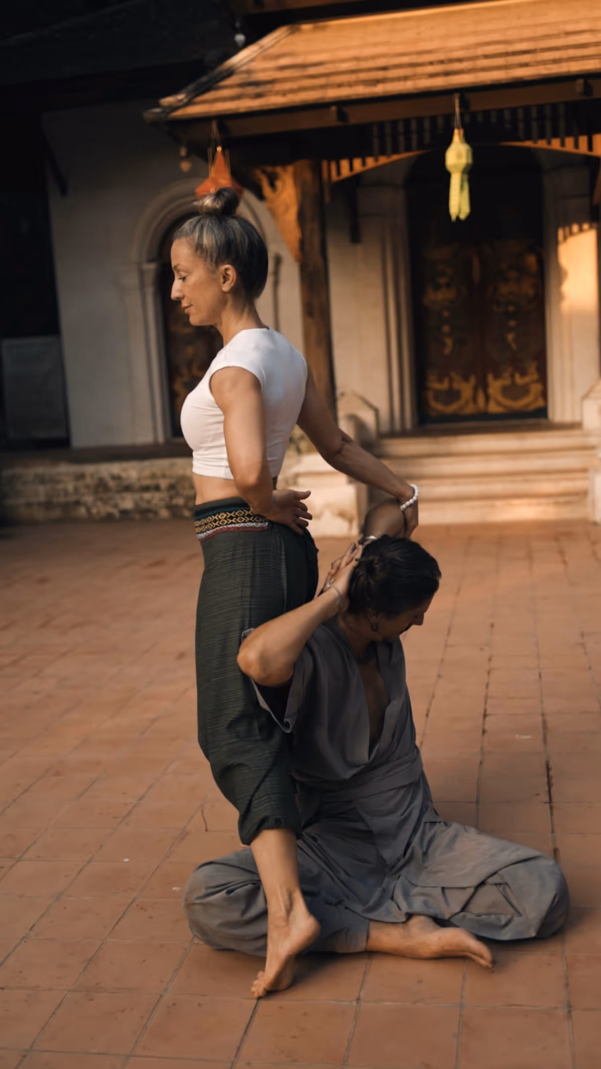 Thai massage therapist stretching client on traditional temple floor