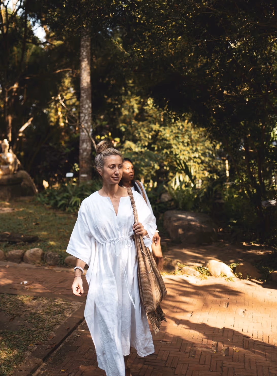 Woman in white dress walking on brick path through sunlit garden