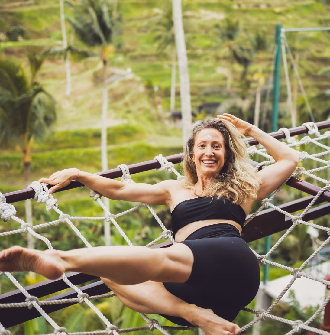 Smiling woman stretching on rope net in lush green outdoor setting