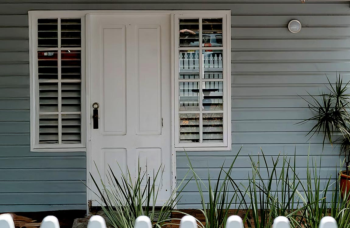 The front veranda of a home, showing the front door, with a window on each side. A QR code to record service can be placed in the window.