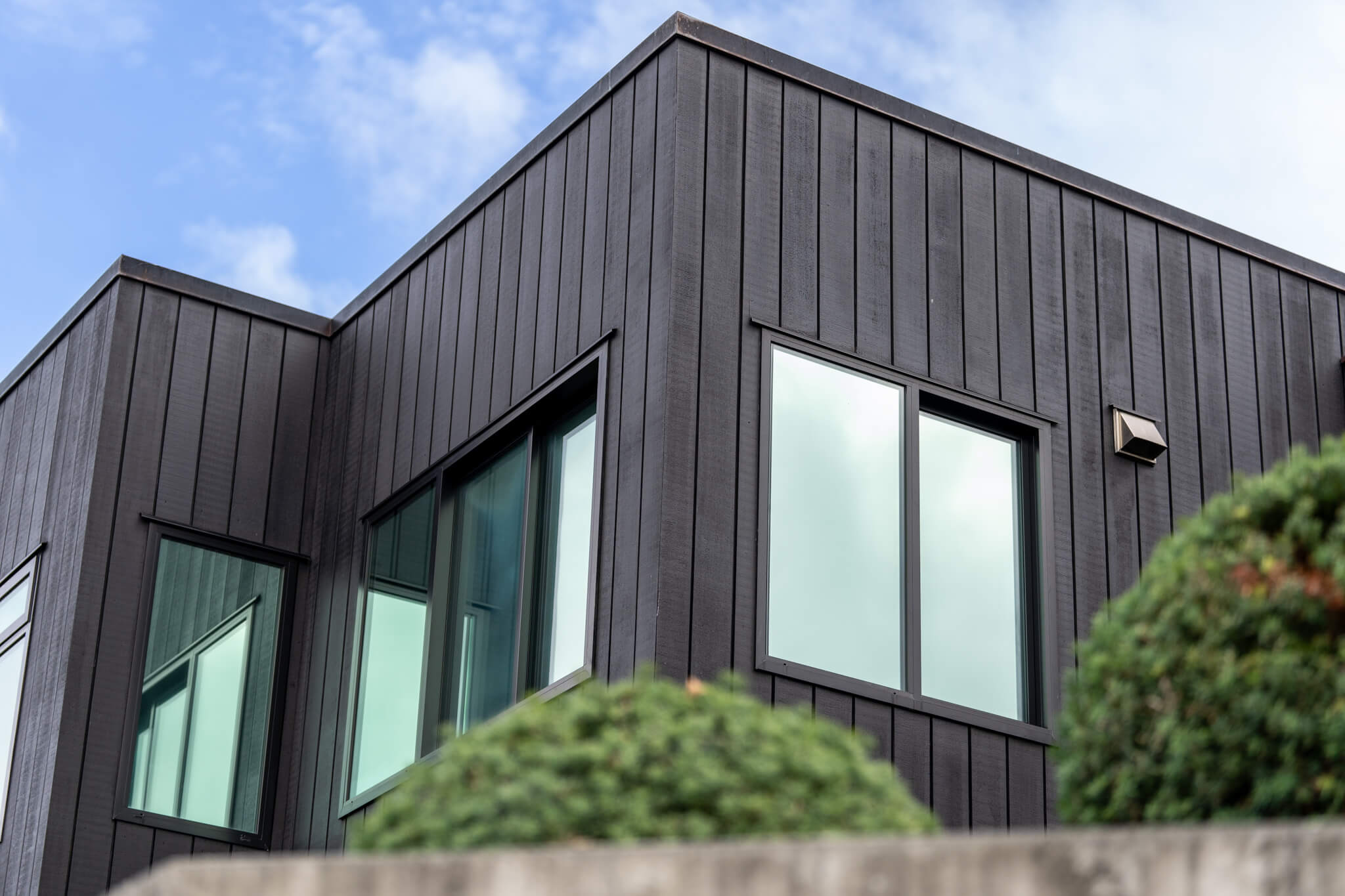 Modern black wooden house exterior with large windows against a blue sky. 