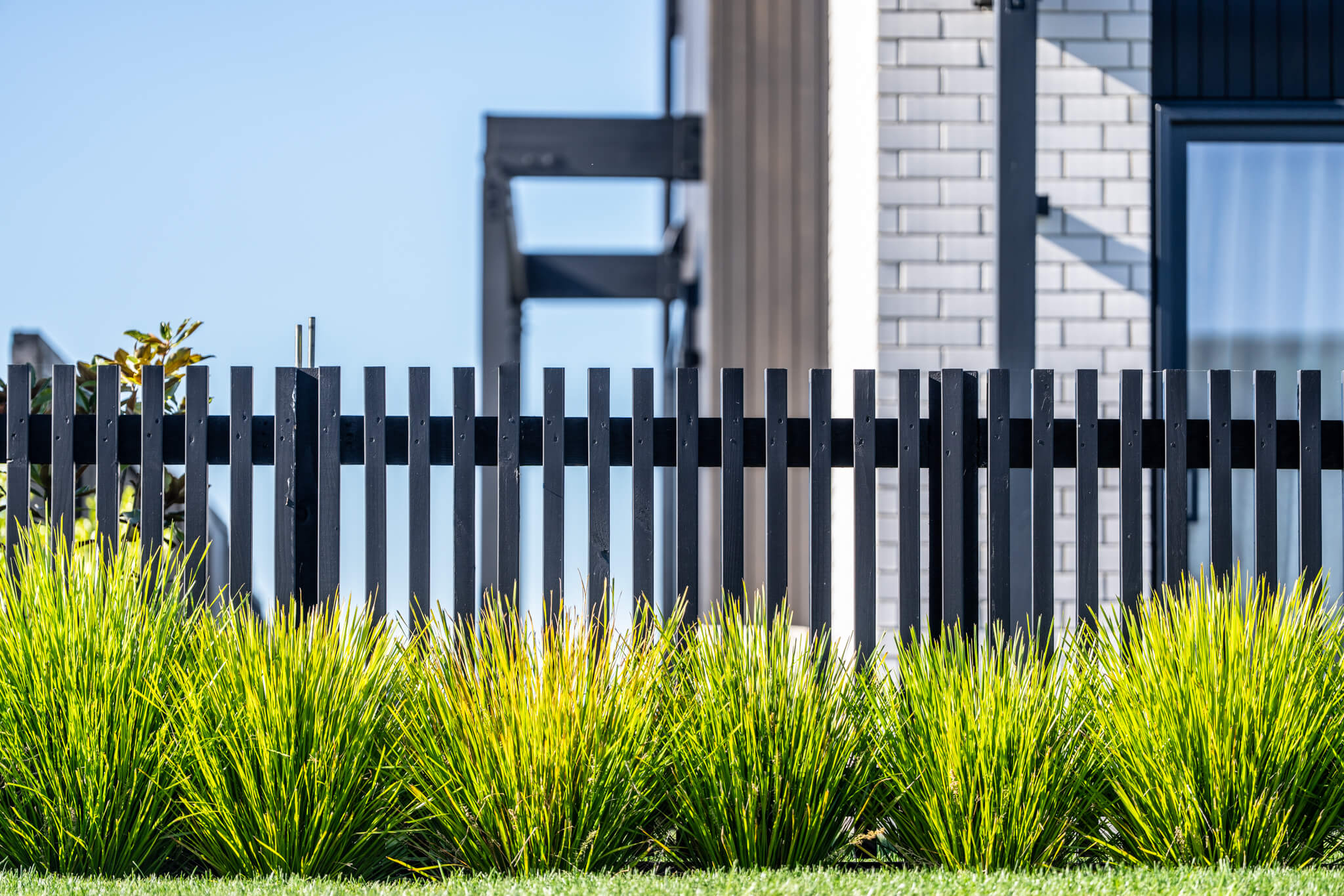 Modern black metal fence with vertical slats, bright green grass and bushes in front.