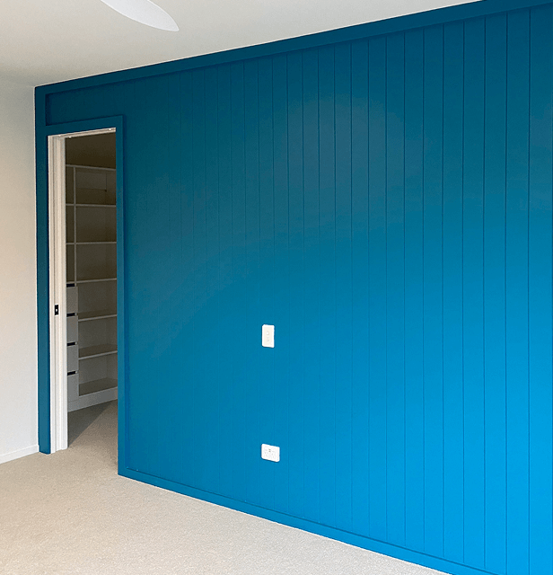 A room features a vibrant blue paneled wall with a light switch and power outlet.