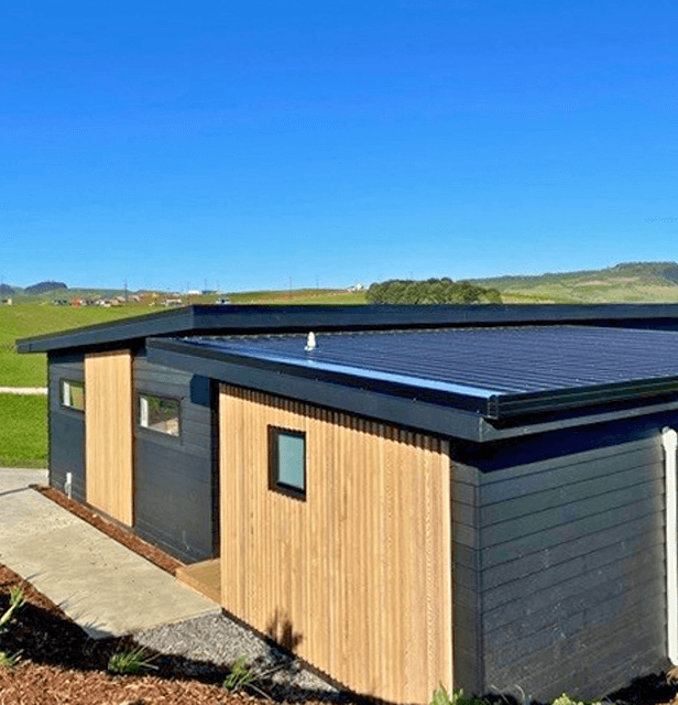 Modern black and wood-paneled house with a flat roof and solar panels.