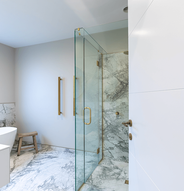 Modern bathroom with glass shower enclosure featuring marble walls and floor. 