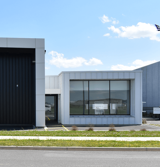 Modern building with contrasting black and white sections, large windows, and a sleek design against a bright blue sky with scattered clouds.
