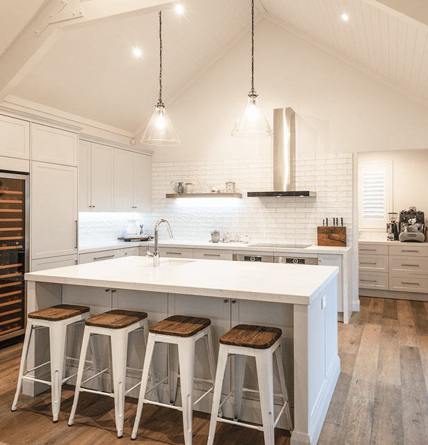Modern farmhouse kitchen with a high ceiling, featuring a white island and four stools