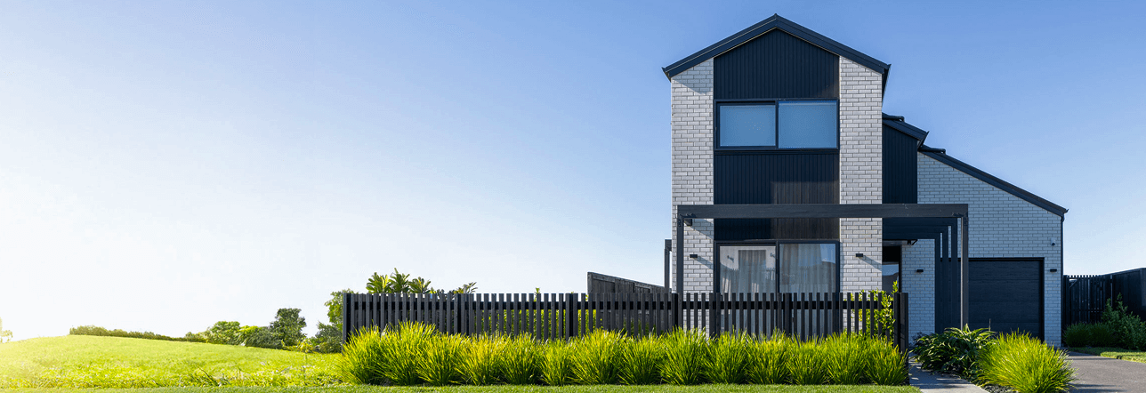 Modern two-story house with a manicured lawn and black fence under clear skies. 