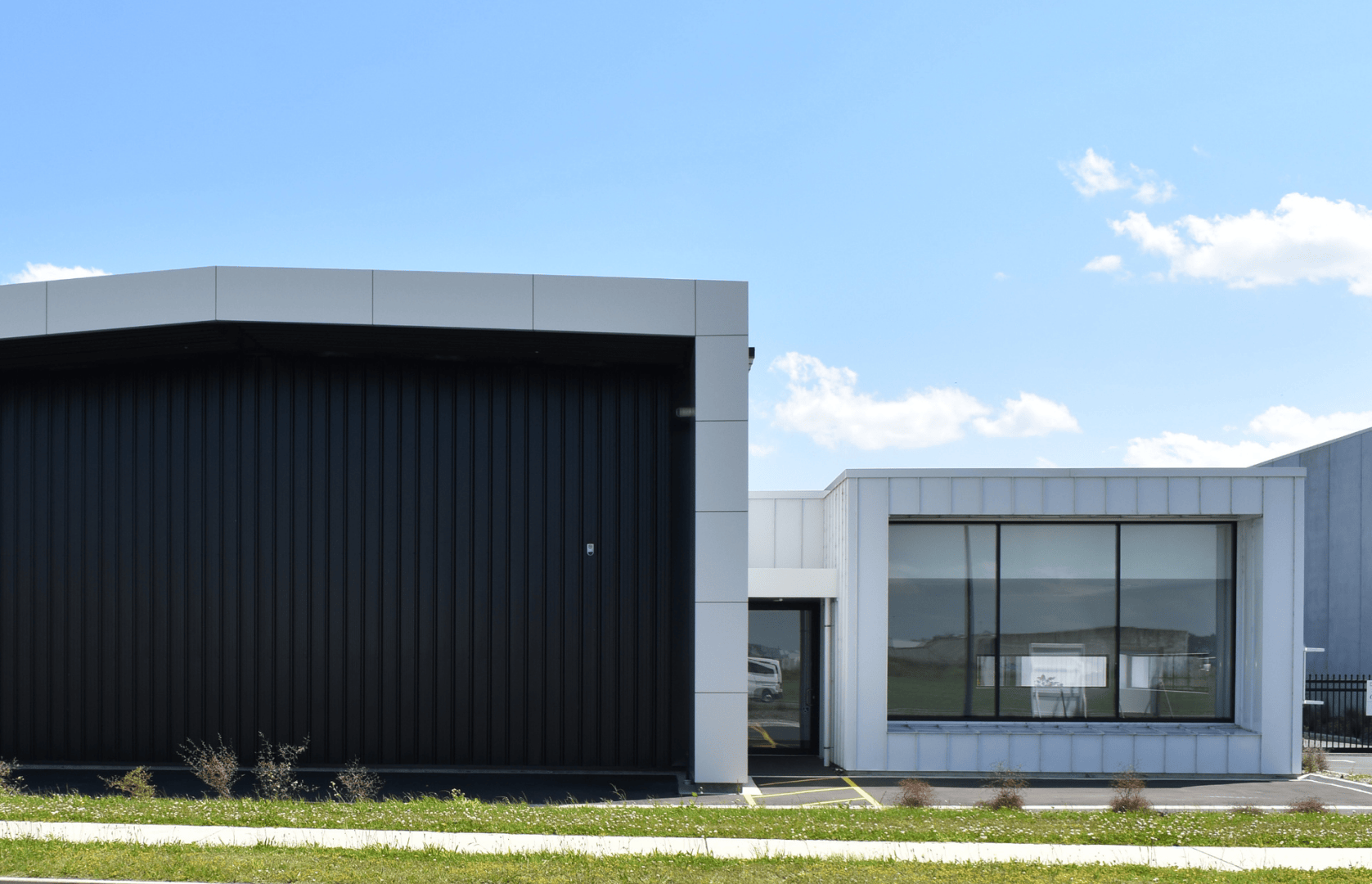 Modern building with contrasting black and white sections, large windows, and a sleek design against a bright blue sky with scattered clouds.