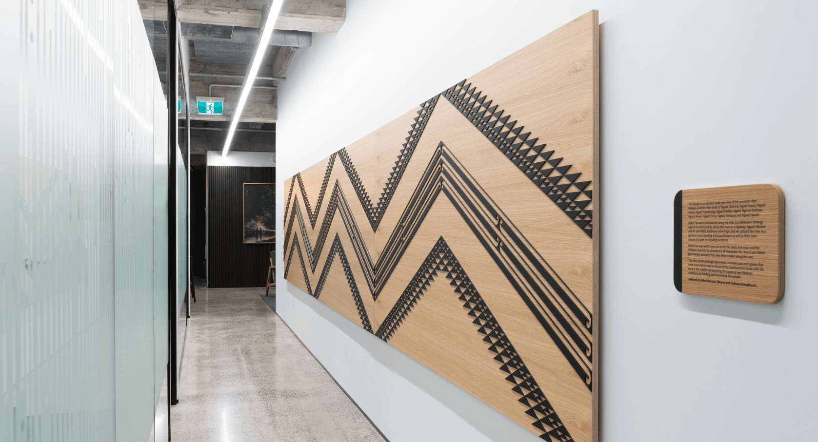 A modern corridor with polished concrete floors and a large wooden panel on the wall featuring bold black zigzag patterns. 