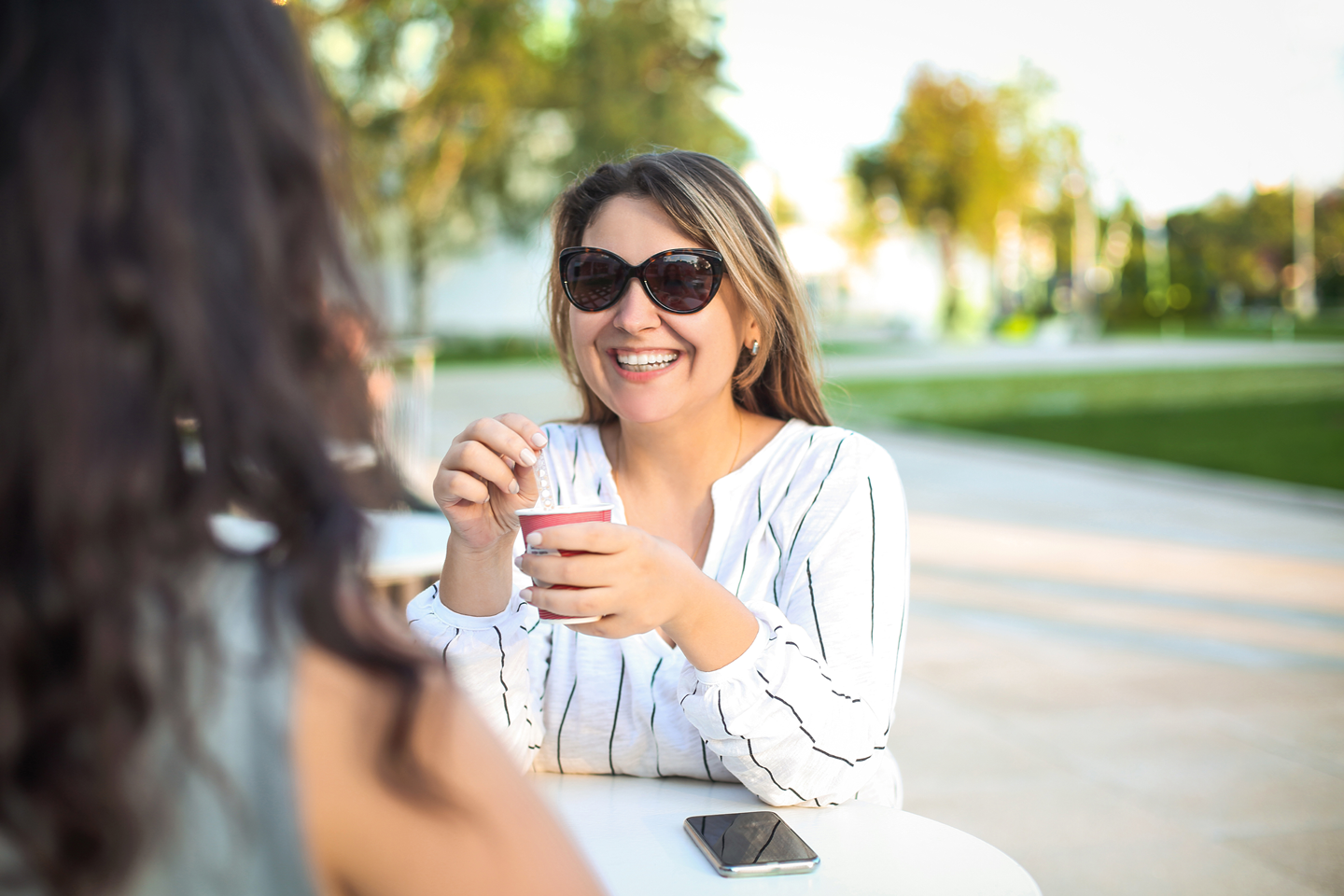 Two women outside drinking coffee at a table.