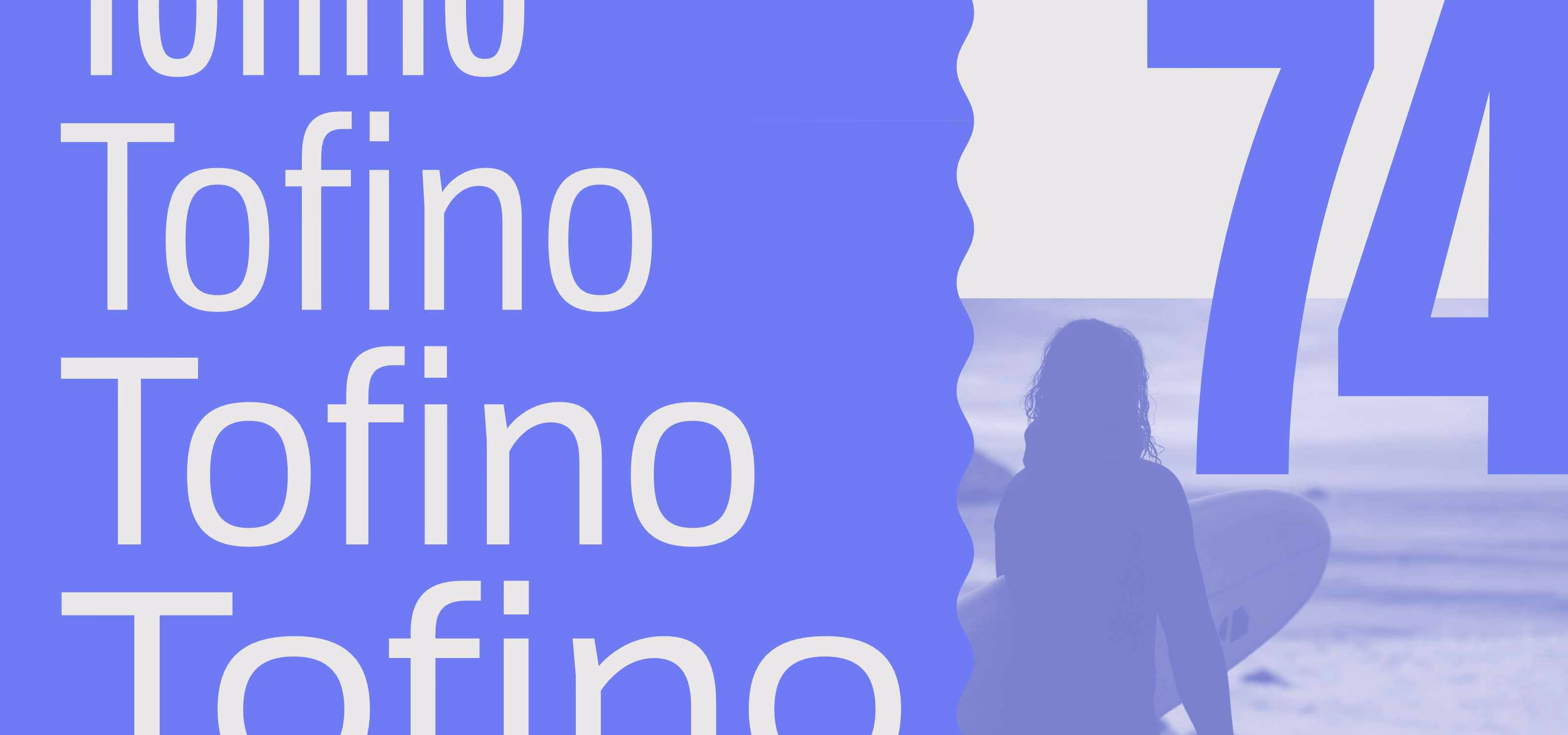 Silhouette of a person holding a surfboard facing the ocean under a large number 74 with the repeated word 'Tofino' on the left side.