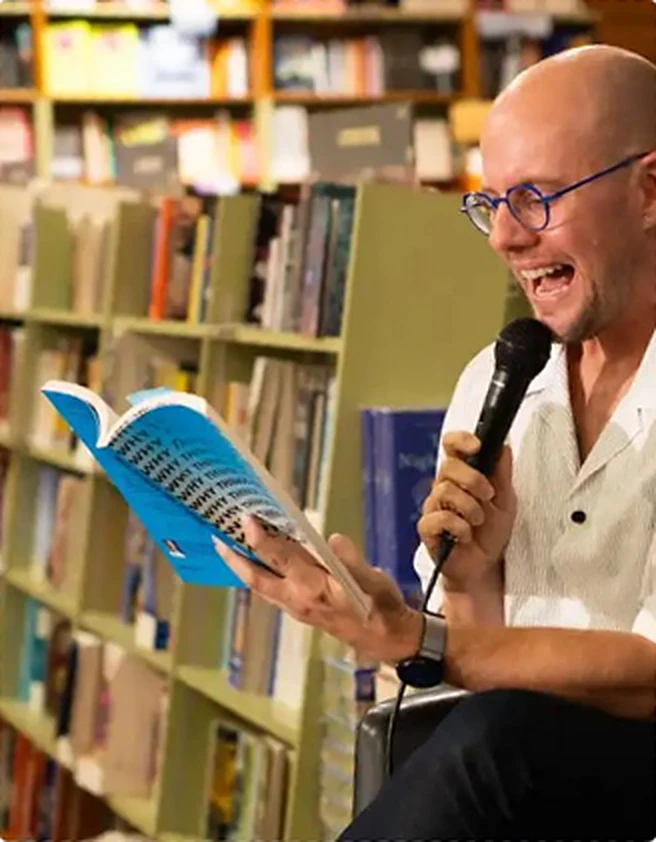 An author laughing as he reads from his book at a bookshop event