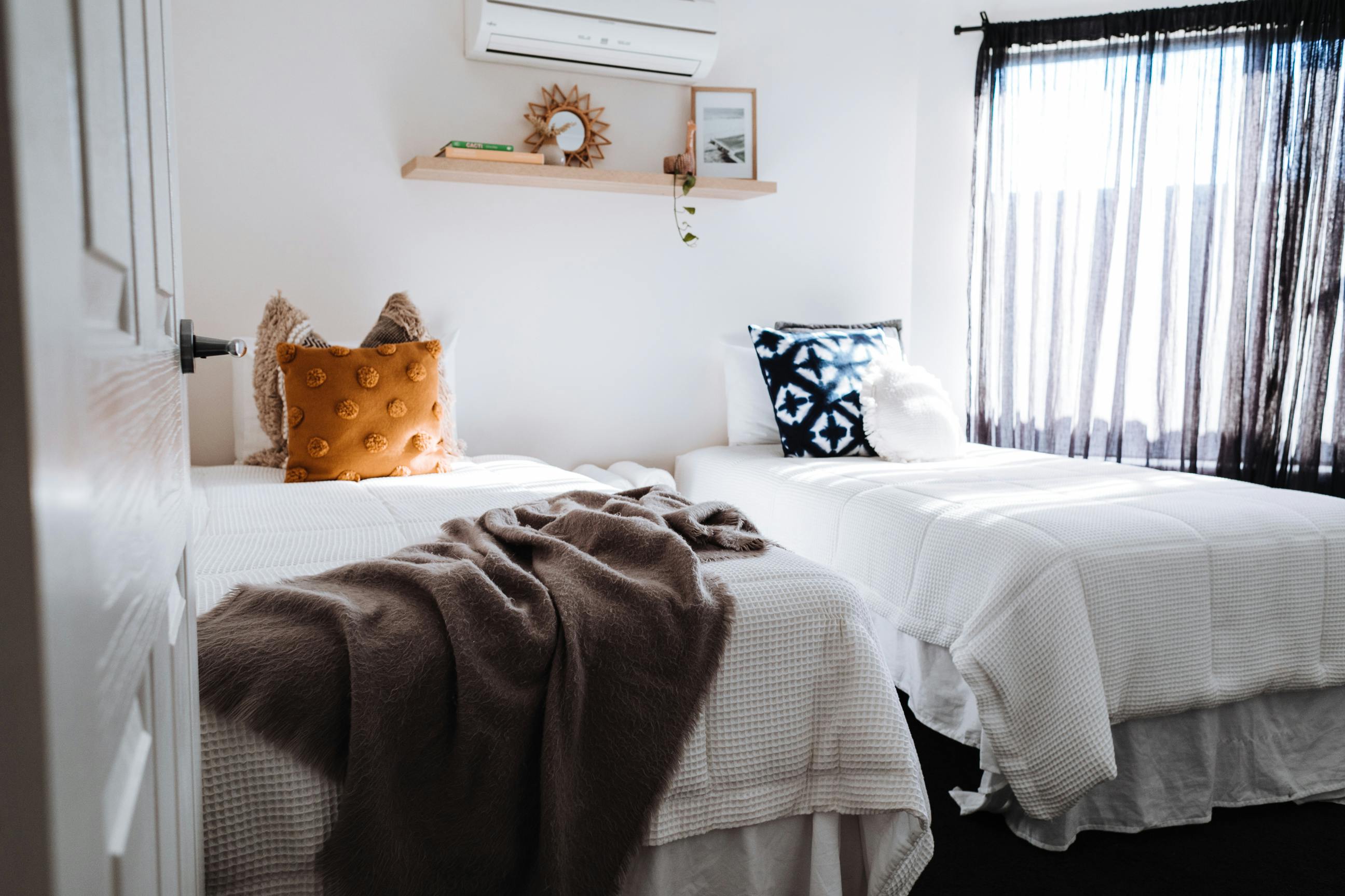 a boho inspired bedroom with twin beds and an air con unit in the middle on the wall